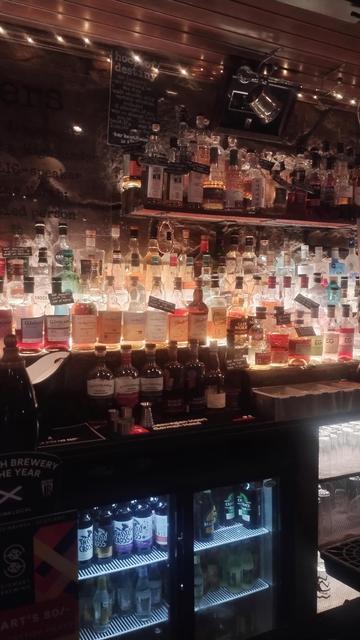 Shelves of single malt whisky bottles, uplit from below so the contents glow, behind the bar at Teuchters