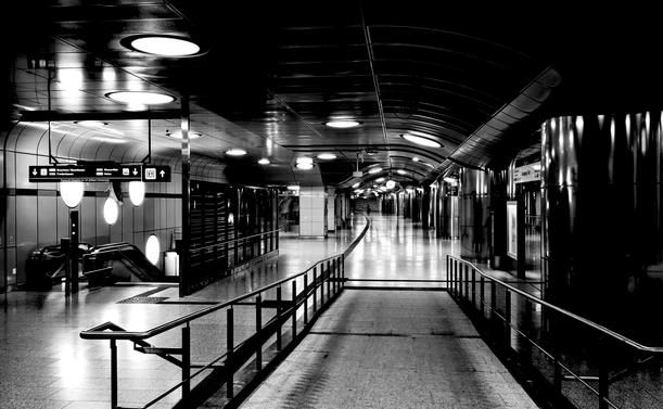 A black and white photo of an empty, modern subway station early morning, featuring curved ceilings, overhead lights, ramps, and escalators.

Ein schwarz-weiss-foto einer leeren, modernen u-bahnstation am fruehen morgen mit gekruemmten decken, oberlichtern, rampen und rolltreppen.