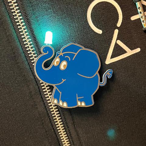 Eine Brosche in Form des blauen Elefanten von "Sendung mit der Maus", der mit seinem Rüssel eine leuchtende LED hält.