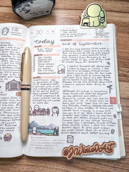 A planner open to a page dated September 30, featuring handwritten notes, tasks, and habits. It includes doodles of characters, a landscape, and various icons. A pen rests on the planner, and a bottle of ink is positioned above it.