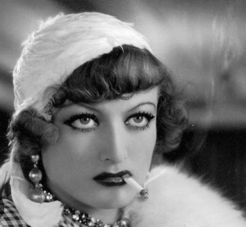 Joan Crawford looking super hot with an aggressive smoky eye, dark lip, and a cigarette hanging out of her lips as she looks intently just off camera.