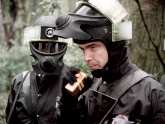 Claude Sonnet 4.0 describes the image as: "I can see two figures in dark tactical or military-style gear in what appears to be a wooded, outdoor setting. One person is wearing a full face mask or helmet with protective equipment, while the other has their face partially visible and is wearing what looks like a tactical helmet or headgear. They appear to be equipped for some kind of mission or operation, with dark clothing and professional-grade protective equipment. The forest setting suggests this might be taking place during a covert operation or military exercise. The lighting and film quality give it a distinctive vintage television production appearance."

Blakes7Bot, version 3.9.33.