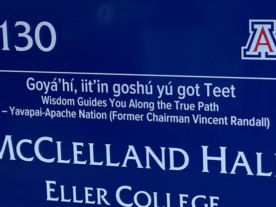 Dark blue sign with white lettering saying "Goyá'hí, iit'in goshú yu got Teet Wisdom Guides you Along the True Path - Yavapai-Apache Nation (Former Chairman Vincent Randall) McClelland Hall, Eller College.