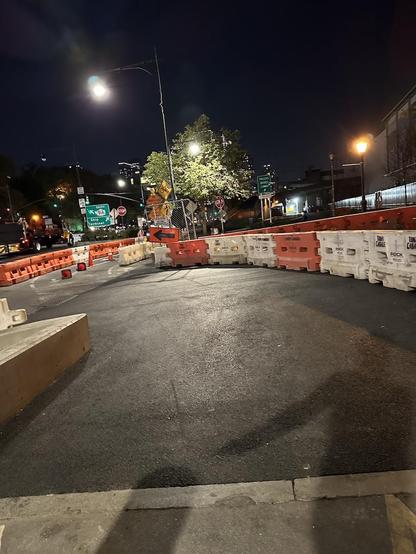 Night-time photo of a bend in a bikepath with very smooth asphalt. There are some plastic barriers at the sides, some cones separating path lanes further head.