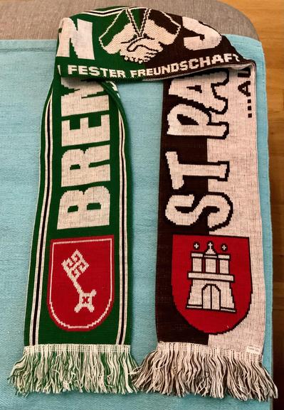 Zu sehen ist ein gemeinsamer Schal zwischen Werder Bremen und den FC St. Pauli. Man sieht beide Schriftzeichen sowie die Wappen der jeweiligen Hansestädte von Bremen und Hamburg, sie in der Mitte zwei Hände und den Schriftzug Fester Freundschaft.
