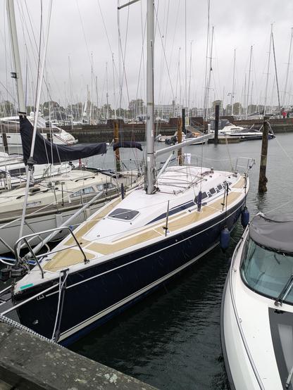 Blue sailboat moored at a marina where the water is low and skies are gray.