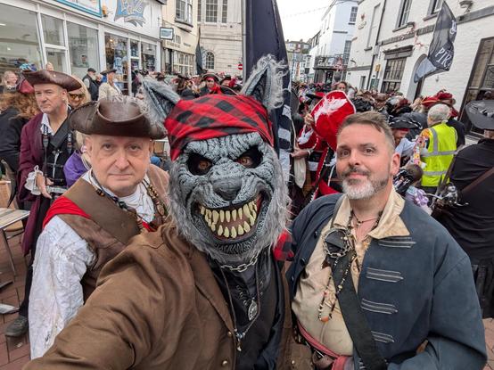 Three Pirates in the foreground on a crowded UK street.  One is a werewolf. A large number of pirates in the background.