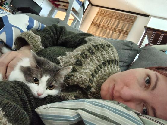 Selfie, jossa ihminen köllöttää sohvalla valkokirjava Helmi-kissa kainalossa.