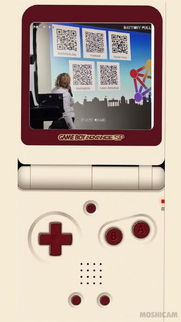 Ein bearbeitetes Bild eines Game Boy Advance SP. Auf dem Bildschirm ist eine Frau mit Mikrofon zu sehen, die auf eine Projektion schaut. Dort sind fünf QR-Codes mit Beschriftungen eingeblendet: „berlinfedi.day“, „Fediwall“, „Starter Pack“, „Mailingliste“ und „Zotero Bibliothek“. Rechts daneben ein buntes, netzwerkartiges Diagramm. Oben im Game-Boy-Rahmen steht „Battery Full“ und „Power On“.