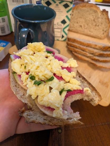 Sourdough bread heapsd with slices of watermelon radish and scrambled eggs