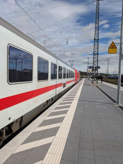 Bahnsteig, grau gepflastert, links sieht man einen IC-Wagen hinter einer roten Lok. Dahinter andere Gleise und der bewölkte Himmel.