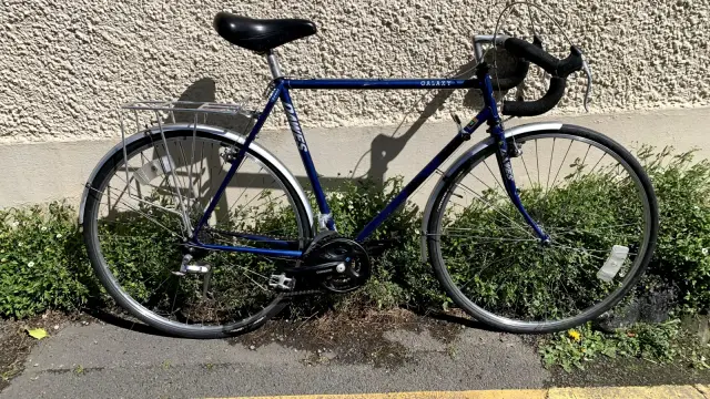 A blue  drop-bar touring bicycle from the late '80s, early '90s. Propped up against a pebbledash wall in the sunshine.