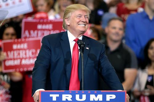 US President Donald Trump smiles as he stands behind a podium while delivering a speech.
