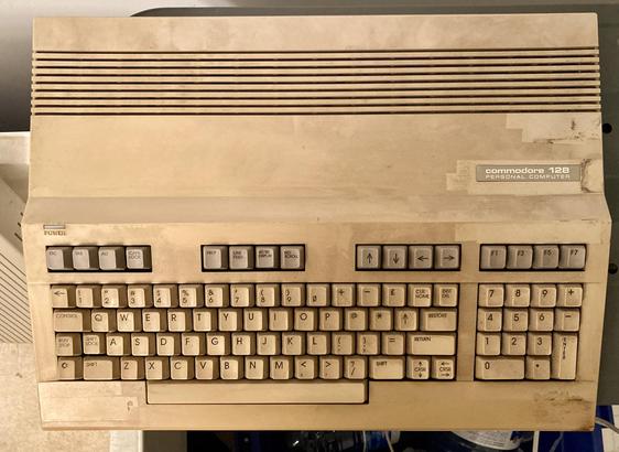 A Commodore 128 computer, waiting to go in the sink and be cleaned. It has very uneven yellowing around some obvious tape marks.