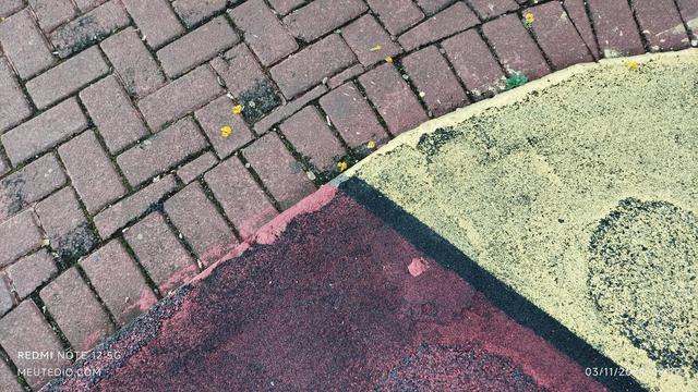 Uma imagem de close-up de uma superfície com textura dividida em duas seções diagonais. A seção superior esquerda é preta e granulada, enquanto a seção inferior direita é amarela e também granulada. A divisão entre as duas seções é diagonal, atravessando a imagem do canto superior direito ao canto inferior esquerdo. Pequenos detritos, como galhos finos ou folhas, estão espalhados em ambas as seções.