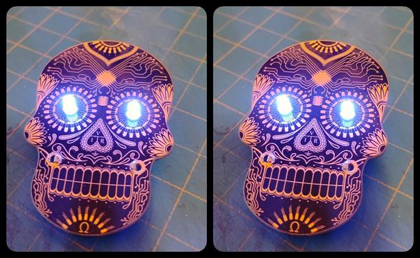 A black and gold circuit board in the style of a Day of the Dead skull, with glowing blue LEDs as eyes. Stereoscopic