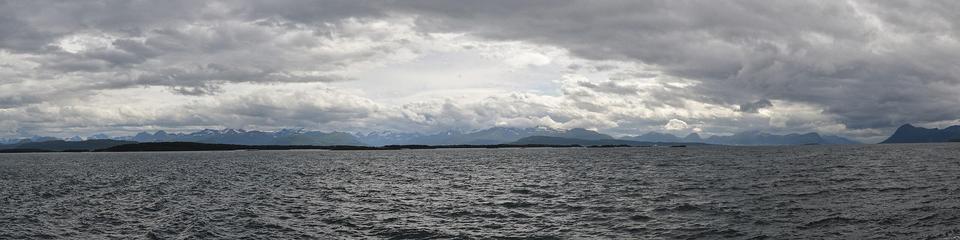 A panoramic photo of a large body of water with mountains on the far shore. The sky is cloudy.