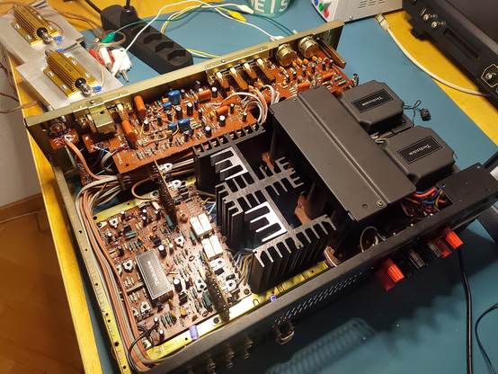 The internals of a Technics SU-8080 hifi amplifier. Rear view. The tone board is at the back, with the mainboard to the left front and the two power transformers and (shrouded) filter cap bank at the rigjt. There are a lot of wires running to and fro, and the center is dominated by and assembly of heat sinks.