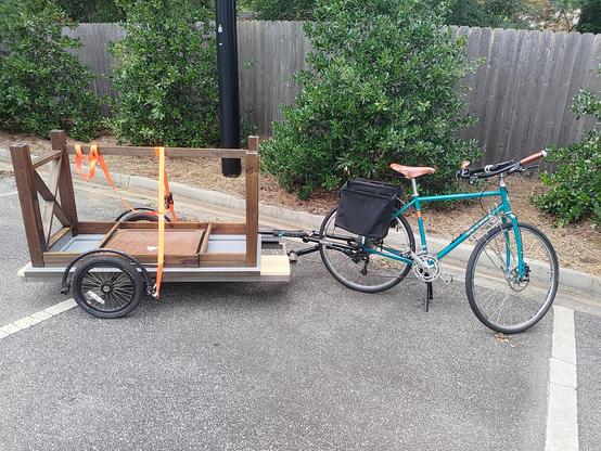A blue bicycle pulling a trailer with a desk on it (upside down, work surface on the trailer).