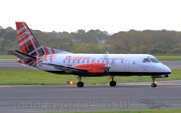Side view of a twin propellor-engined airliner taxiing along a black taxiway from left to right.
The plane is largely white, with a black belly, and the black letters "NG" above the cockpit windows, repeatedin white on the open nose-weheel doors.
There are black "Scotlands Airline" titles on the upper forward fuselage, with larger, red "LoganAir" titles on the upper rear.
The black registration "G-GNG" is on the lower rear fuselage, partially obscured by the wing.
The rear fuselage and tail is covered in a red, black, and white tartan.
The engine pods on the wings are a bright red.
Black taxiway fills the foreground, lined by green grass.
A black runway stretches across the background, with trees leading off into the distance, under bright but hazy sky.