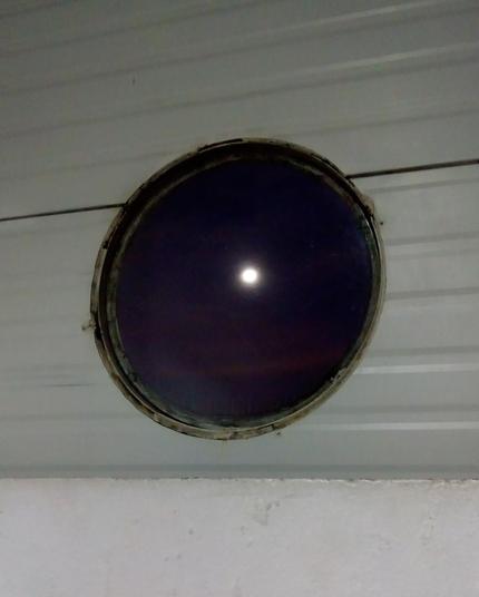 Foto de janela redonda, vista para o céu do anoitecer e a lua mais ou menos no centro.
