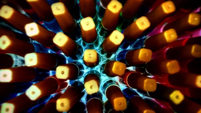 Um close-up abstrato mostra uma vista de cima para baixo de esmaltes com fundos quadrados, que emitem uma luz amarela brilhante. Os esmaltes são de várias cores na parte de baixo, incluindo azul, vermelho e tons mais escuros. As pontas quadradas iluminadas criam um padrão repetitivo e hipnotizante.