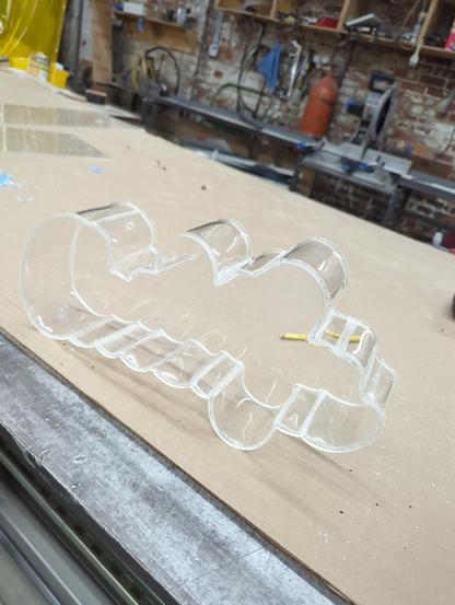 a clar acrylic channel letter on a metal and cardboard table. The letters are a curvy outline of a word made dimensional with a bent acrylic return and a backer plate
