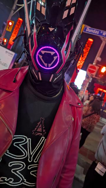 GAMMA, a drone wearing a black shirt and a magenta jacket, with a black, purple, and pink cyberpunk-themed mask.
