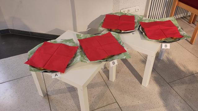 2 kleine weiße Tische mit vier runden Tabletts darauf. Die Tabletts sind mit roten Servietten abgedeckt.
