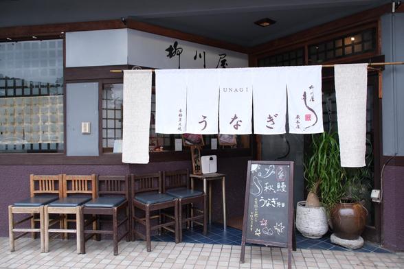The front of the eel restaurant. White short curtain hanging that says unagi, or eel yin Japanese, with an illustration of an eel