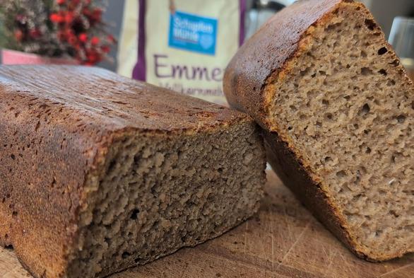 Angeschnittenes Vollkorn-Kastenbrot, im Hintergrund eine Mehltüte mit Schriftzug "Emmer"