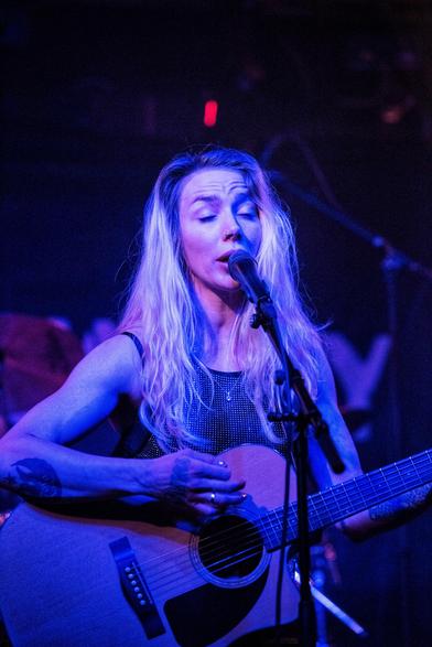 Eine Frau singt mit geschlossenen Augen und spielt dabei eine Akustikgitarre.