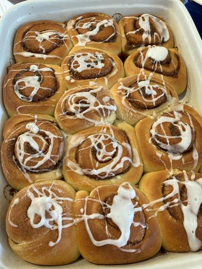 Weiße Backform gefüllt mit Zimtschnecken die mit Zuckerguss verziert wurden