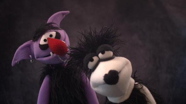 Two goth hand puppets, a large live hands purple ogre and a white fleece Greeblee with black lipstick