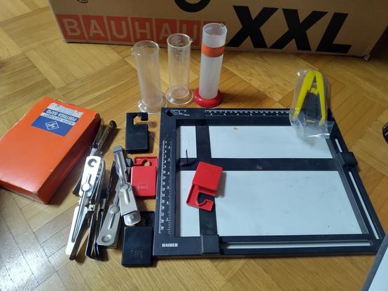 Zubehör bestehend aus Klammern, Messkolben, Zange zum Anziehen von Feuchtigkeit, eine Art Zeichenbrett zur Größenabmessung und antikes Fotopapier in einem orangenen Karton