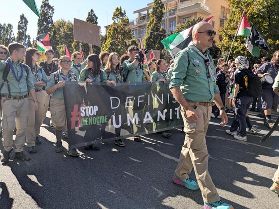 Un gruppo di scout marcia all'interno del corteo tenendo uno striscione su cui si leggono le scritte "stop genocide" e "definisci umanità".