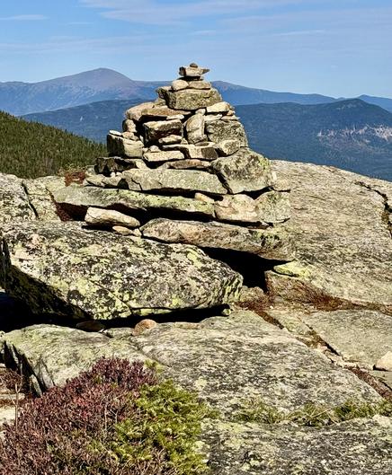 Pile of rocks (cairn) in shape of cone on rocky top of mountain. Expansive view of mountain range off in the distance. Red and green alpine vegetation in foreground. Blue sky overhead. 

This is the summit of Bondcliff Mountain that I hiked to two days ago on my backpacking trip to the White Mountains, New Hampshire. The highest peak in the distance is Mount Washington.