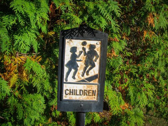 A black and white metal sign with a boy and girl playing with a ball, labeled "Children"