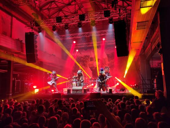 Vier Dinosaurier und ein Drache rocken auf einer Bühne.