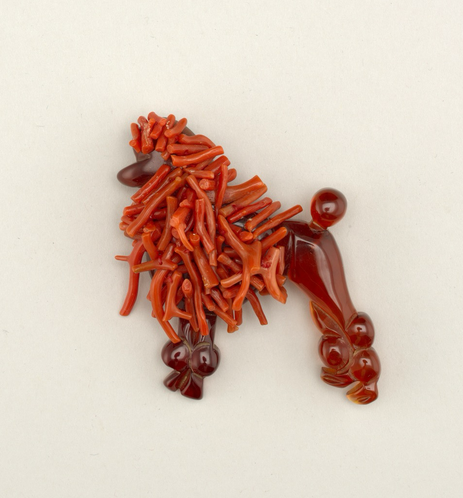 official museum photo of the object, front view on white background red brooch in the form of a poodle, with plastic body and coral pieces used for the fur