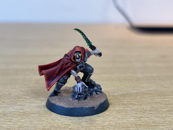 Genestealer Cults Sanctus miniature painted with a red robe, yellow goggles and a green blade.
