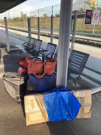 Empty Track at Besançon TGV Station. A couple of benches and in front our luggage - a covered foldable bike, three bike bags, a big blue suitcase with a handbag propped on top, and a huuuge flat cardboard box with a cut open ikea bag to carry it.