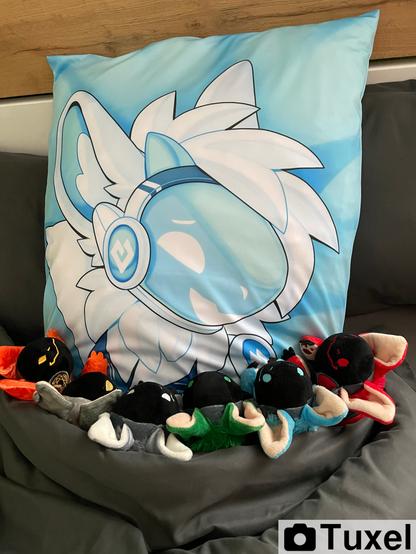 Big pillow with a protogem print under a blanket, only head ans shoulders are showing. At the edge of the blanket on top of the big pillow there a sitting six protobean plushies. It looks like they are cuddling the big pillow.