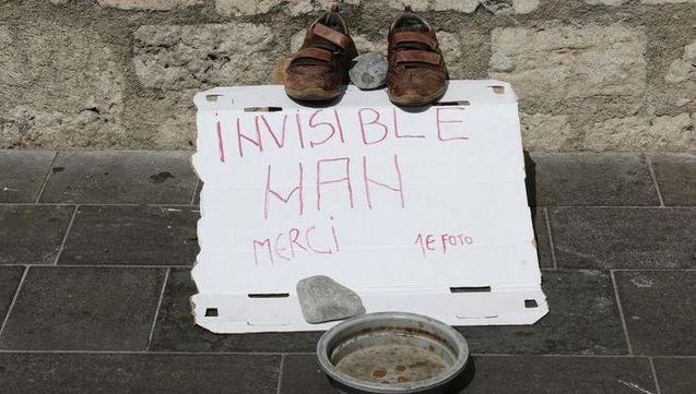 Une pancarte où est inscrit "invisible man, merci, 1€ foto" (homme invisible, merci 1€ pour une photo)
Au-dessus de la carte, une paire de sandales
Sous la pancarte, une coupelle avec quelques centimes