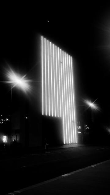 Vertical shoebox of a building at night, with multiple vertical lines of lights on its front