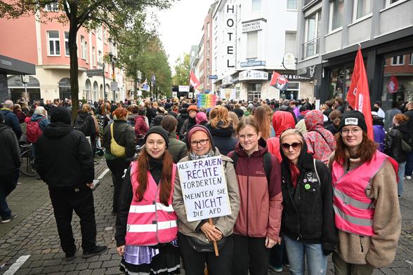 5 Flintas lächeln in die Camera. Im Hintergrund ist die Demo gegen den 1000-kreuze-marsch zu sehen. viele menschen von hinten.