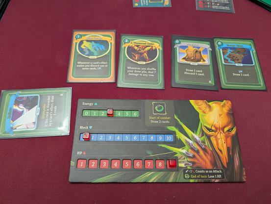 Close up of The Silent's playerboard and a few cards. After Image provides block when a card causes you to discard, which is good, but not necessary for infinite. Everything is used, though: A Thousand Cuts causes damage when you shuffle, Prepared lets you draw one then discard one for free, Escape Plan lets you draw a card for free, and Reflex lets you draw cards if it's discarded. Loop them together until you've shuffled your way to victory!