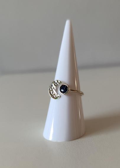 a ring with a dark blue stone and a silver half moon. it's placed on a white cone