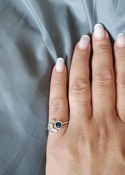 a ring with a dark blue stone and a silver half moon. it's worn by a woman in her hand