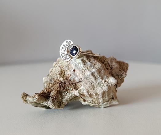 a ring with a dark blue stone and a silver half moon. it's placed on a seashell